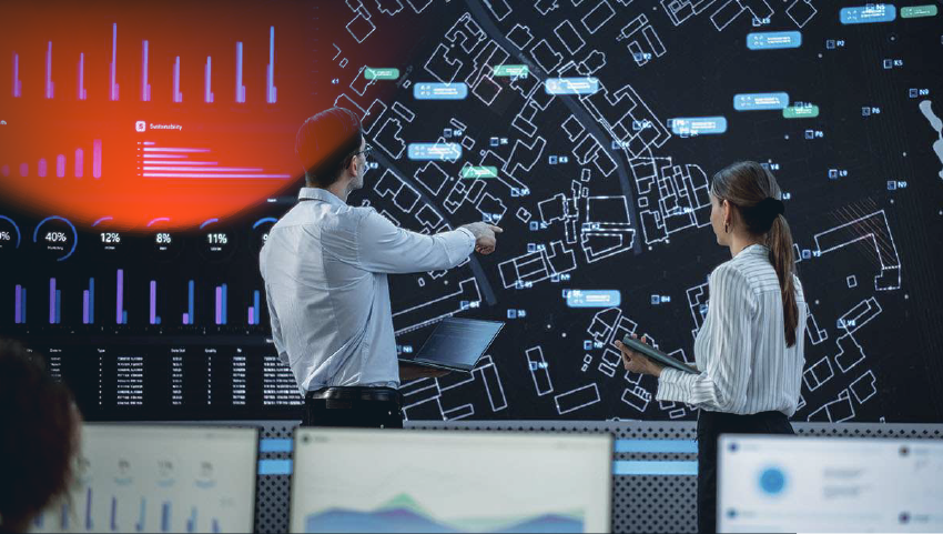 Male And Female Logistics Specialists Discussing New Routs Of Delivery In Front Of Big Digital Screen In Monitoring Office