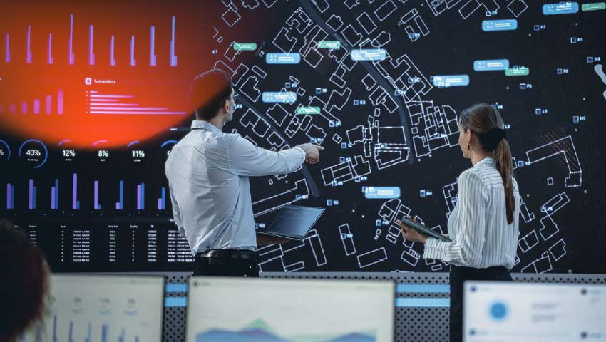 Male And Female Logistics Specialists Discussing New Routs Of Delivery In Front Of Big Digital Screen In Monitoring Office